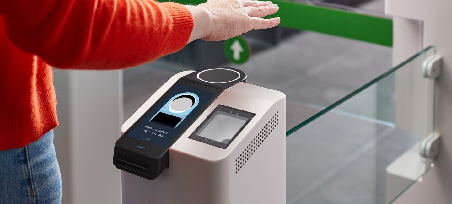 A person stands at a grocery entry gate with their hand suspended over a palm reading device. 